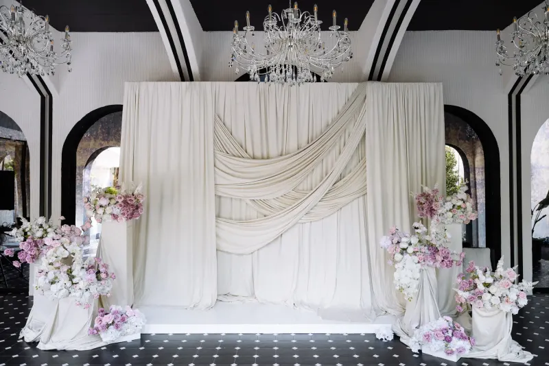 Arcada de ceremonie din sala Noir, cu draperii crem, flori și candelabru